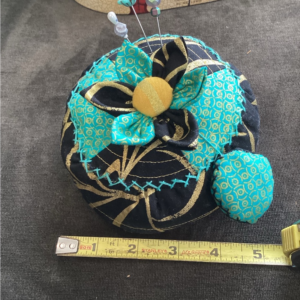 Boutique: large pin cushion with three decorative pins and emery sharpening pad.